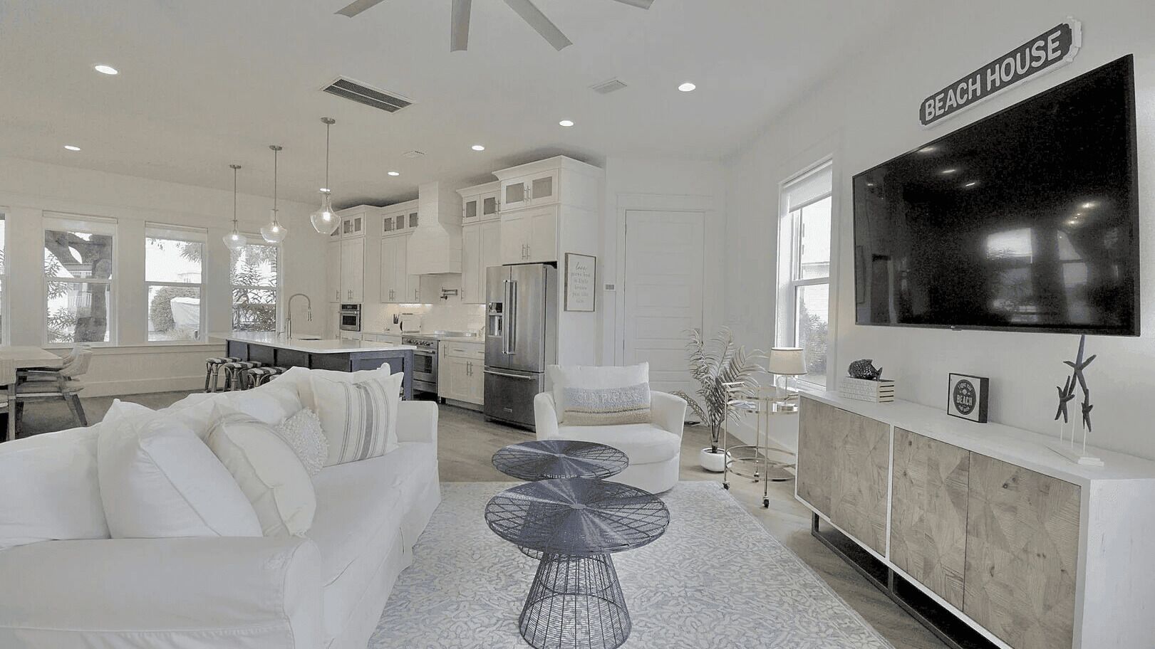 A modern kitchen with white cabinets, a large refrigerator, and a dining area with a white table and chairs.