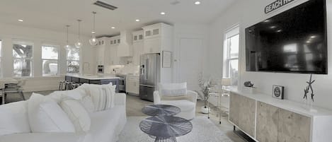 A modern kitchen with white cabinets, a large refrigerator, and a dining area with a white table and chairs.
