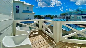 A wooden deck with white chairs, a pool area, and buildings in the background. - Jessa Blu by Avantstay Walk to Beach Pool + Gym (Santa Rosa Beach)
