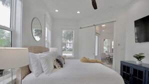 A modern bedroom with a large bed, a bedside lamp, a mirror, and a TV on the wall. - Jessa Blu by Avantstay Walk to Beach Pool + Gym (Santa Rosa Beach)