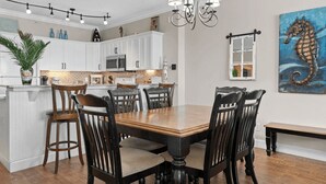 A modern kitchen with white cabinets, a wooden dining table, and a chandelier. - Emerald Isle Resort 405 by Avantstay Beachfront, Beach Chairs + Pool Access (Panama City Beach)