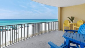A balcony with a view of a beach, yellow chairs, and a small table with a plant. - Emerald Isle Resort 405 by Avantstay Beachfront, Beach Chairs + Pool Access (Panama City Beach)