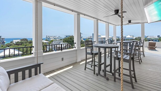 Eine überdachte Terrasse im Freien mit Tisch und Stühlen, die einen malerischen Blick auf das Meer und die Gebäude bietet.