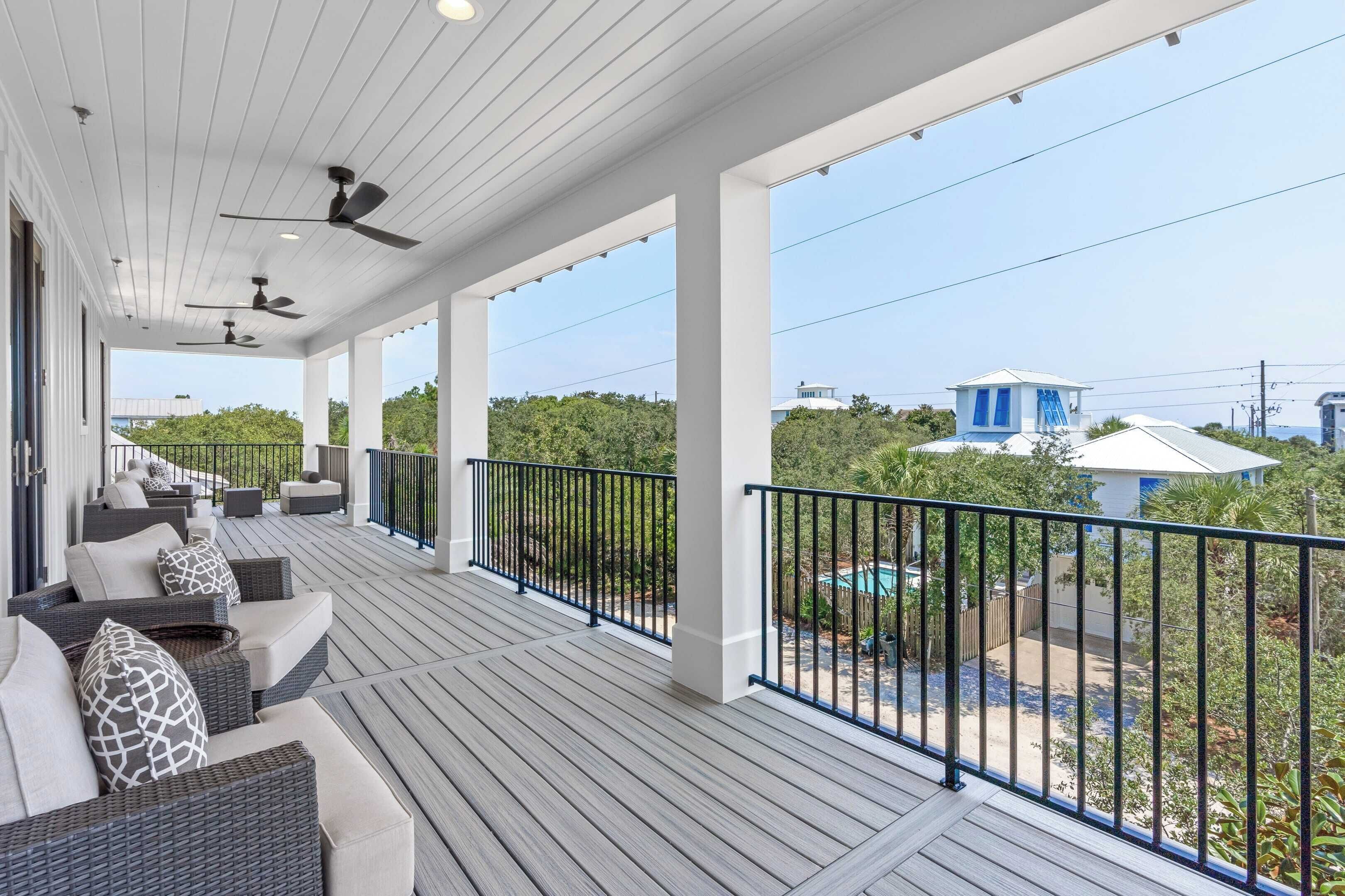 A covered outdoor area with ceiling fans, a wooden deck, and outdoor seating.