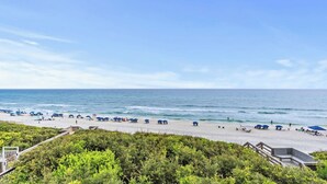 Une plage avec des parasols et des gens, une terrasse en bois et une vue sur l’océan.