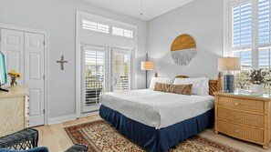 A bedroom with a bed, dresser, lamp, and a wall-mounted circular decoration. - Grovey by the Sea by Avantstay Oceanfront, Private Beach, Pool Access (Santa Rosa Beach)