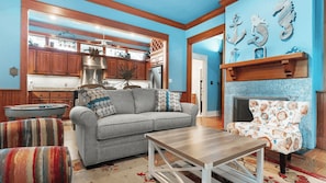 A living room with a sofa, armchair, and coffee table. There is a fireplace with a patterned rug.