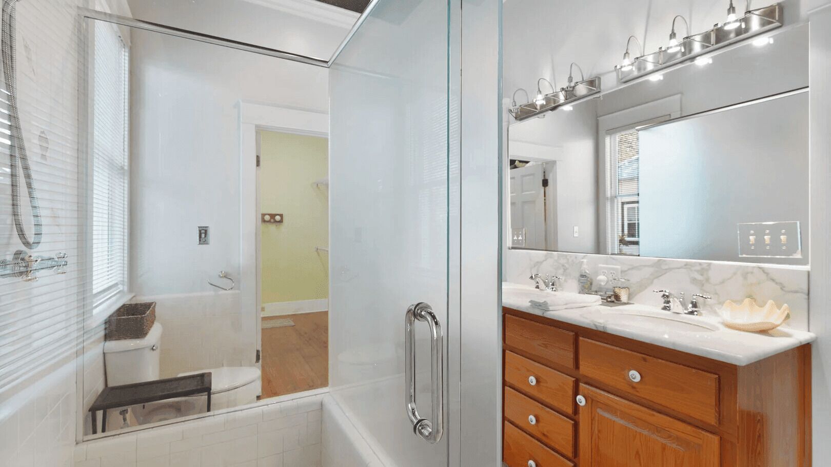 Une salle de bain moderne dotée d’une douche à parois de verre, d’un meuble-lavabo avec un plan de travail en marbre et d’un grand miroir au-dessus du lavabo.