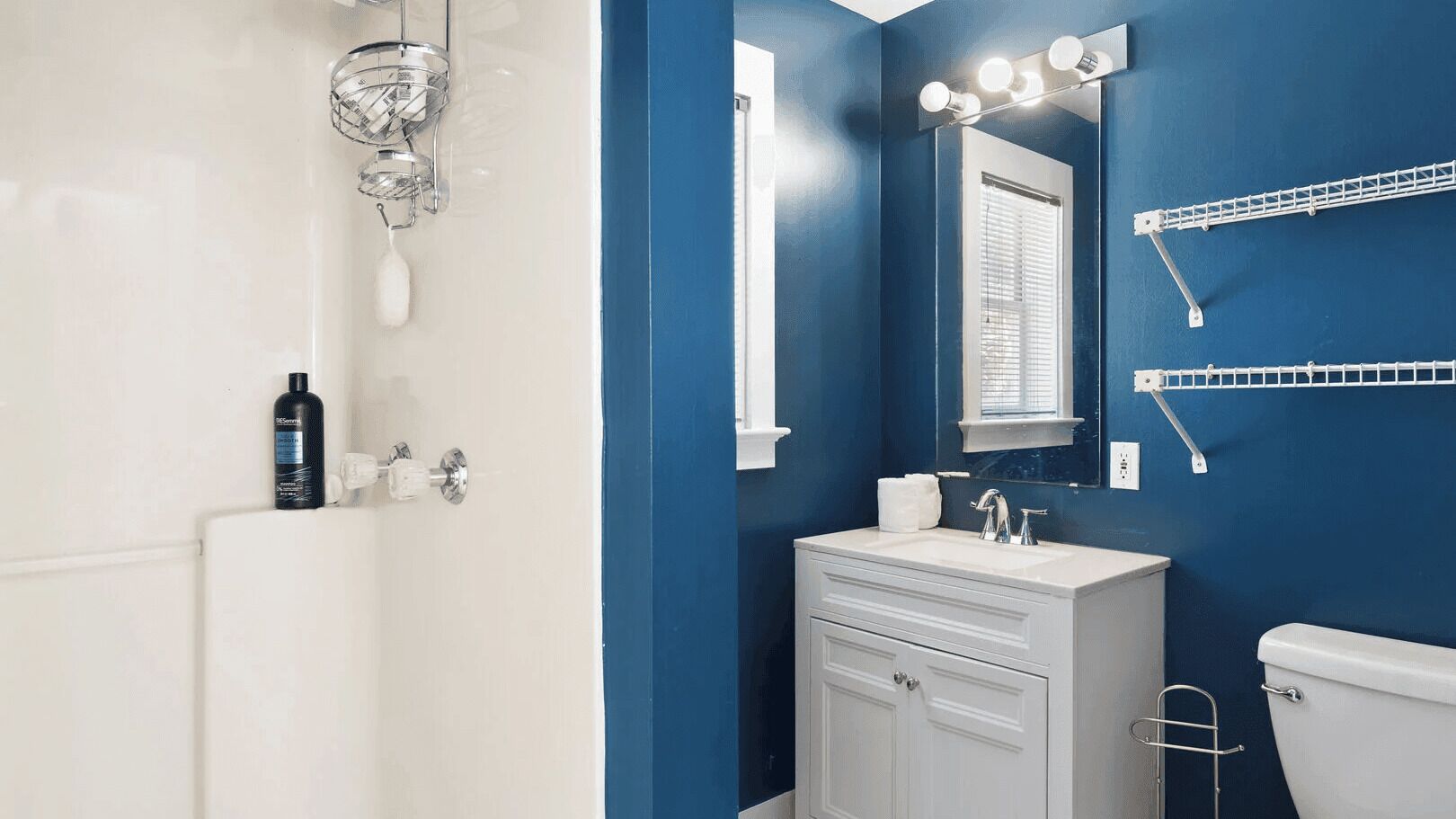 Un baño con una bañera blanca, un lavamanos blanco, un espejo con luces y una pared azul.