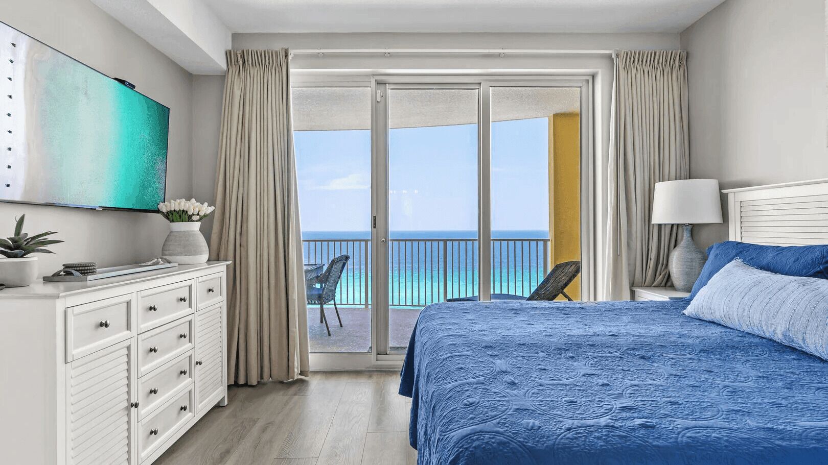 A bedroom with a bed, a dresser, a TV, and a view of the ocean.