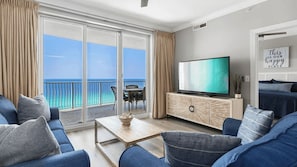 Een moderne woonkamer met een grote televisie, een bank, een salontafel en uitzicht op de oceaan.