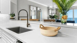 Une cuisine moderne avec un plan de travail blanc, un évier, un bol décoratif et une plante en pot.