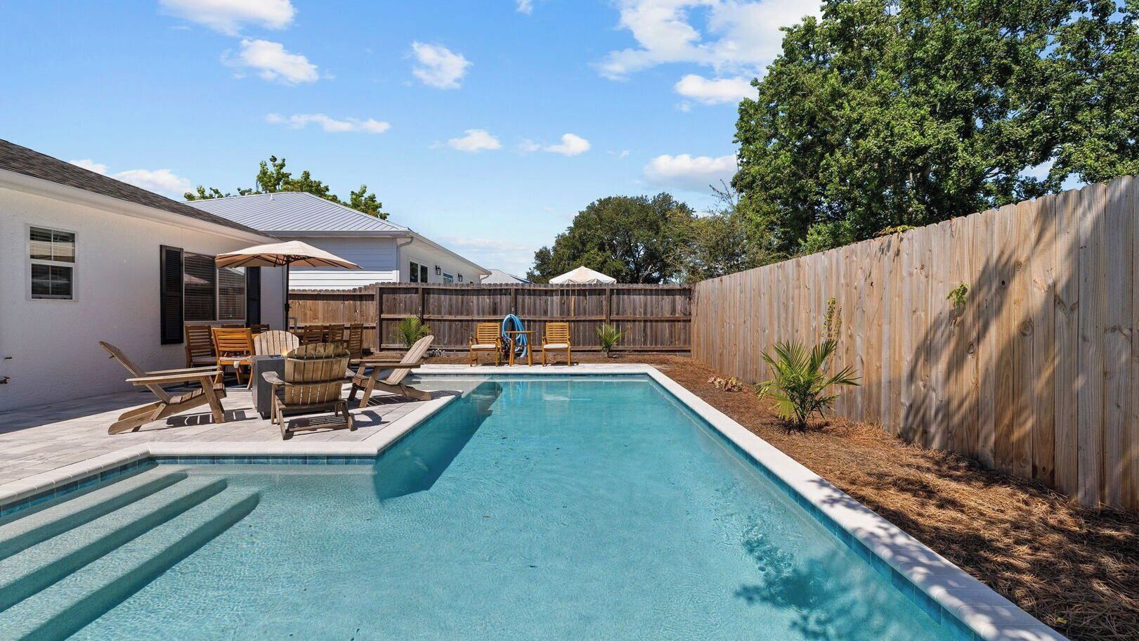 A rectangular swimming pool with steps leading into it, surrounded by a wooden fence.