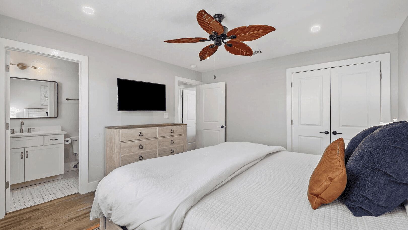 A bedroom with a bed, a dresser, a television, and a ceiling fan.