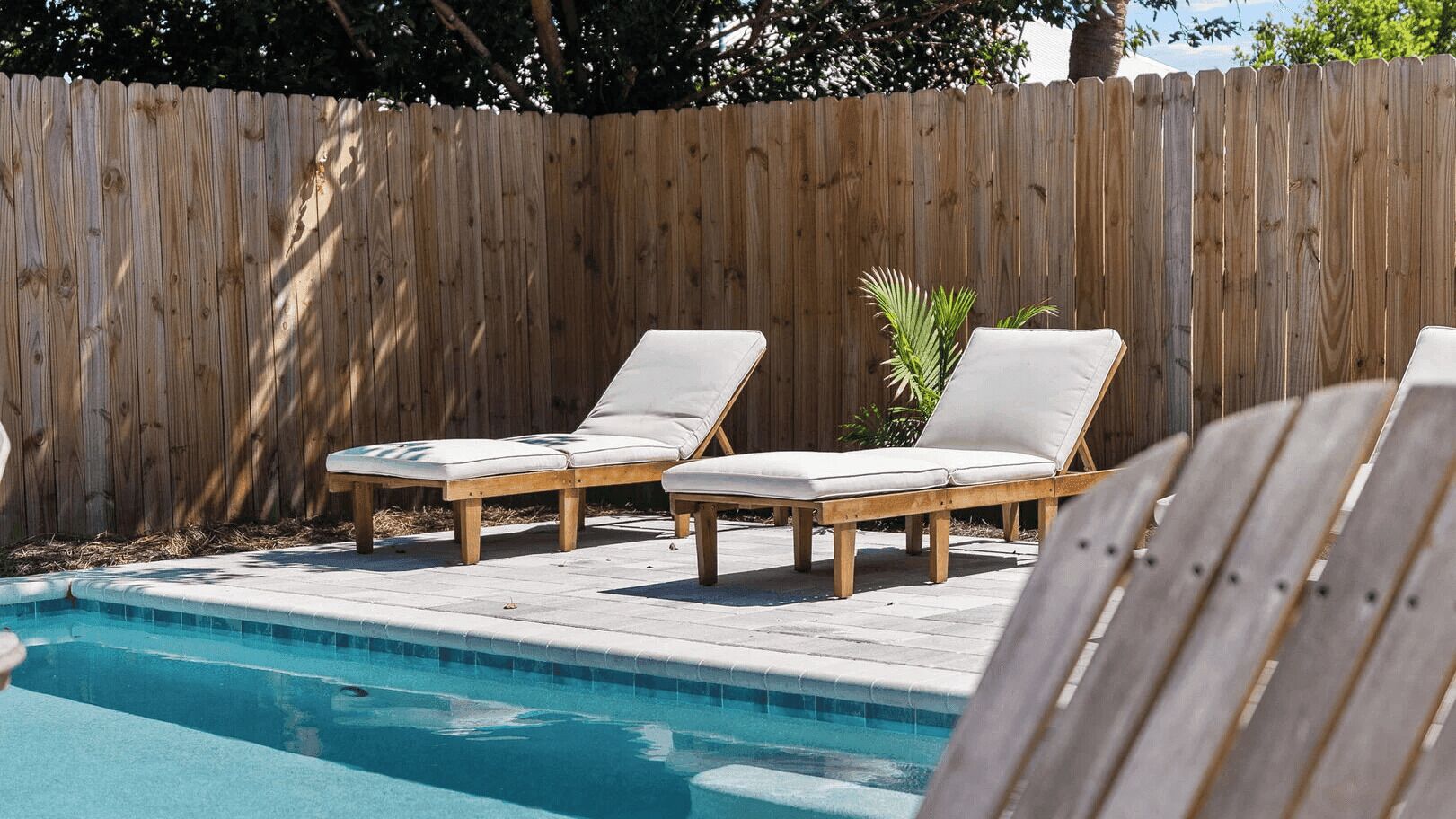 A pool with two wooden lounge chairs.