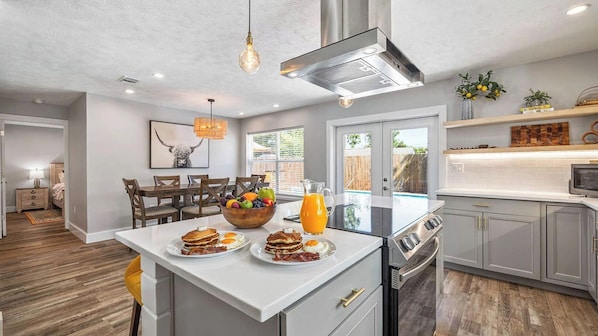 A modern kitchen with a central island, stainless steel appliances, and a dining area with wooden chairs.