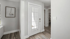 Um corredor com uma porta branca, piso de madeira e um quadro pendurado na parede.