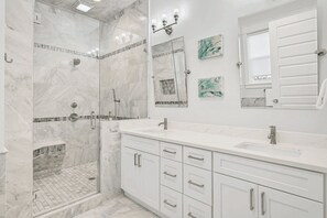 A modern bathroom with a glass-enclosed shower, white marble tiles, a large mirror, and a vanity with drawers. - Alibi 30A by Avantstay 6bdr, Private Pool, Steps to Beach (Panama City Beach)