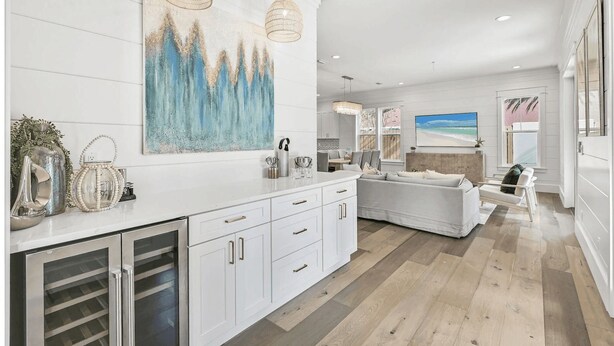 Una cocina moderna con armarios blancos, una isla grande, luces colgantes y un cuadro de una playa.