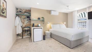 Una habitación de hotel moderna con una cama, un escritorio pequeño con cafetera, aire acondicionado de pared y una planta decorativa.