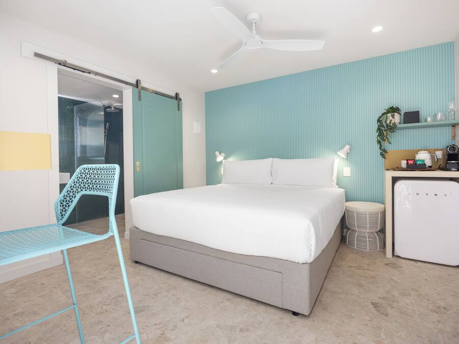 A bedroom with a bed, a desk, a chair, a ceiling fan, and a small refrigerator.