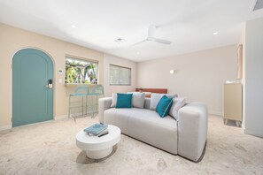 Ein modernes Wohnzimmer mit einer Couch, zwei Sesseln, einem Couchtisch, einem Deckenventilator und einer Tür.