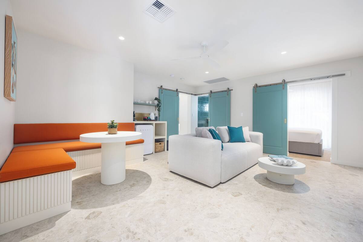 Un salon moderne avec un canapé blanc, un banc orange et une table basse ronde.