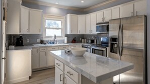 Cocina moderna con armarios blancos, electrodomésticos de acero inoxidable y una isla grande con un bol.