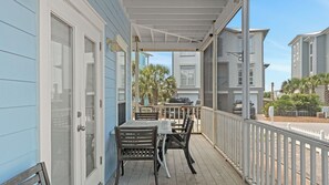A covered outdoor area with a table and chairs, a white railing, and a view of neighboring buildings. - Holiday House by Avantstay Oceanview, Steps to Beach (Santa Rosa Beach)