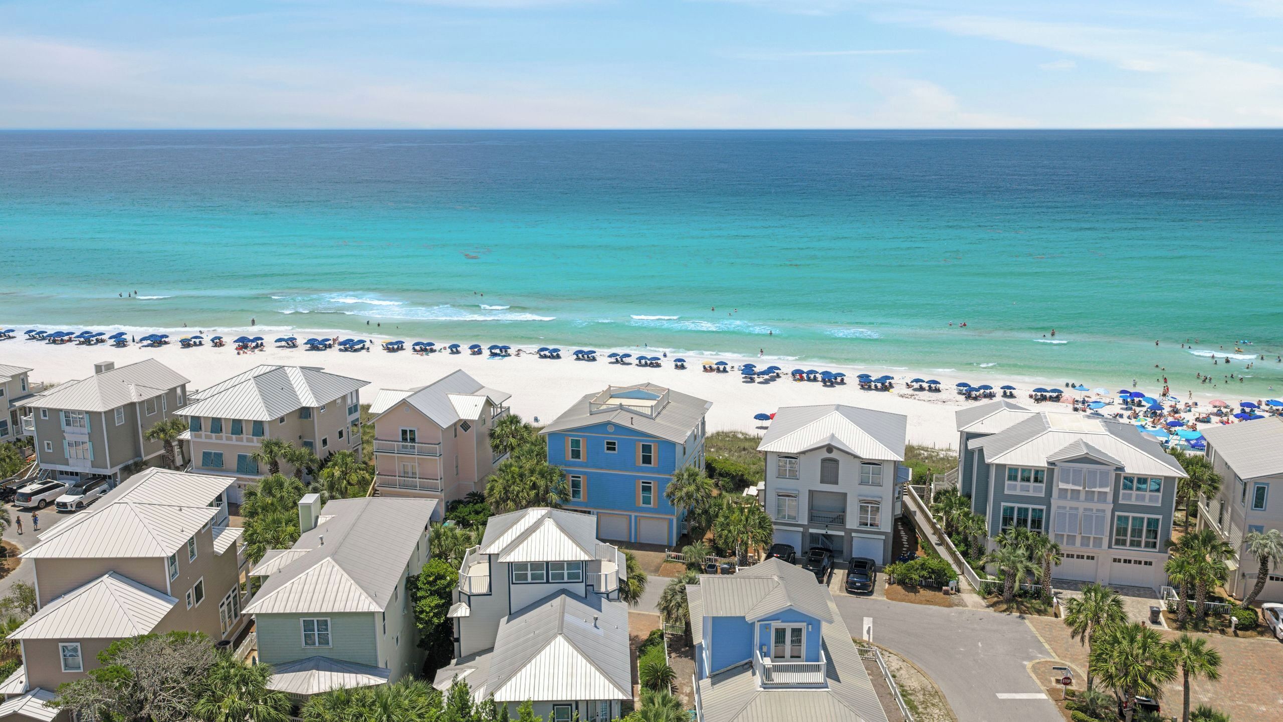 A beachfront hotel with multiple-story buildings, a sandy beach with umbrellas, and the ocean in the background.