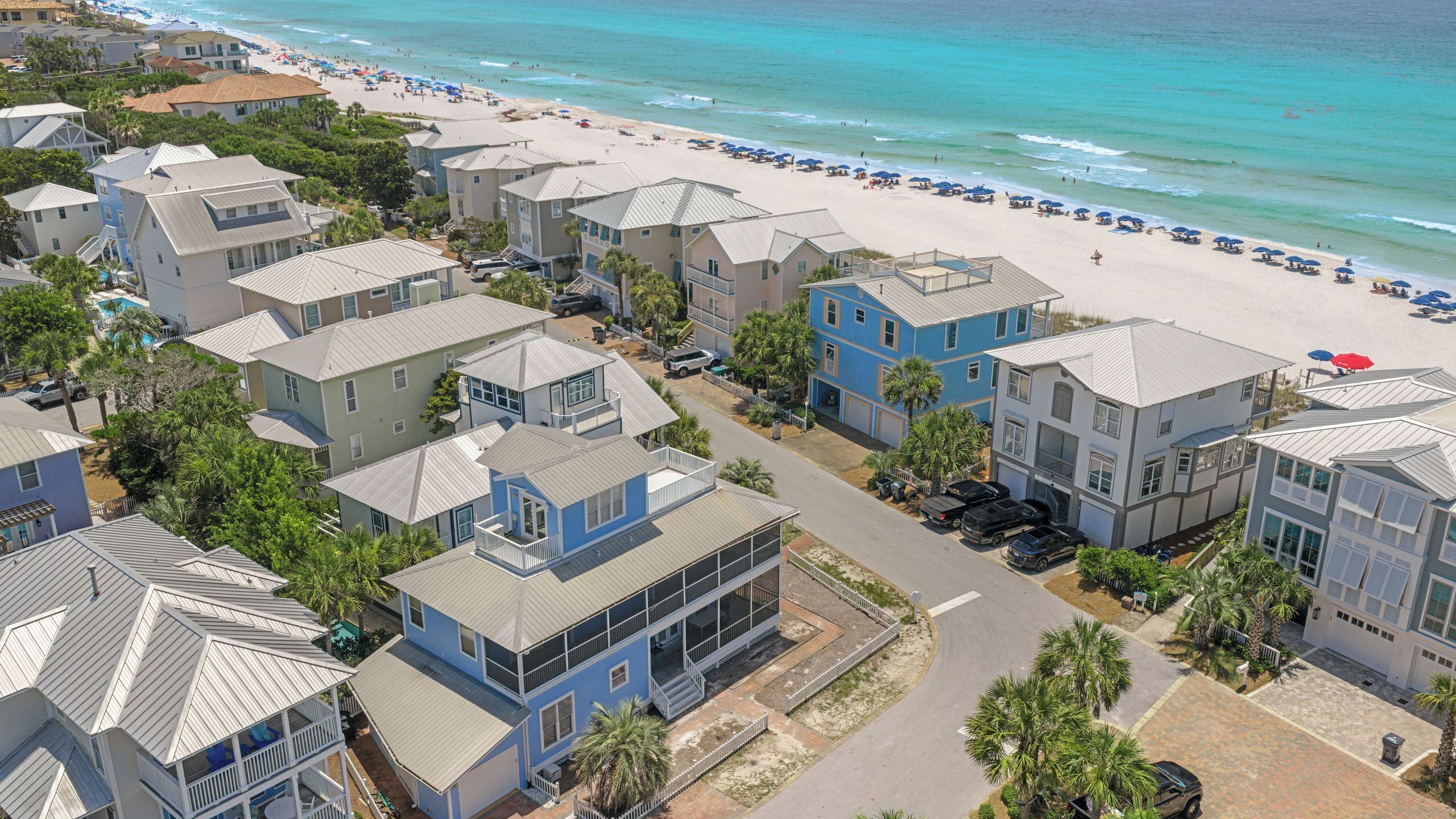 Un quartier résidentiel situé sur la côte, avec des propriétés donnant sur la plage, notamment des maisons dotées de balcons et une plage équipée de parasols.