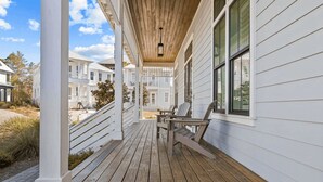A wooden deck with Adirondack chairs, a covered porch, and a view of neighboring houses. - 30A Aqua Vista by Avantstay Golf Cart Included, Pool Acess, Walk to Beach (Santa Rosa Beach)