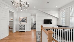 A spacious living area with a wooden staircase, a chandelier, and a television mounted on the wall. - 30A Aqua Vista by Avantstay Golf Cart Included, Pool Acess, Walk to Beach (Santa Rosa Beach)