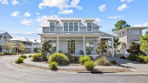 A two-story house with a porch, surrounded by landscaped gardens and a paved driveway. - 30A Aqua Vista by Avantstay Golf Cart Included, Pool Acess, Walk to Beach (Santa Rosa Beach)