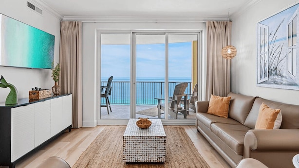A spacious living room with a large sliding glass door leading to a balcony with a view of the ocean. - Coastal Hippy Chic by Avantstay Oceanfront, 2 Pools, Beach Chairs Incl (Panama City Beach)