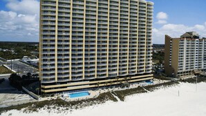 A high-rise hotel with multiple balconies, a swimming pool, and a beach view.