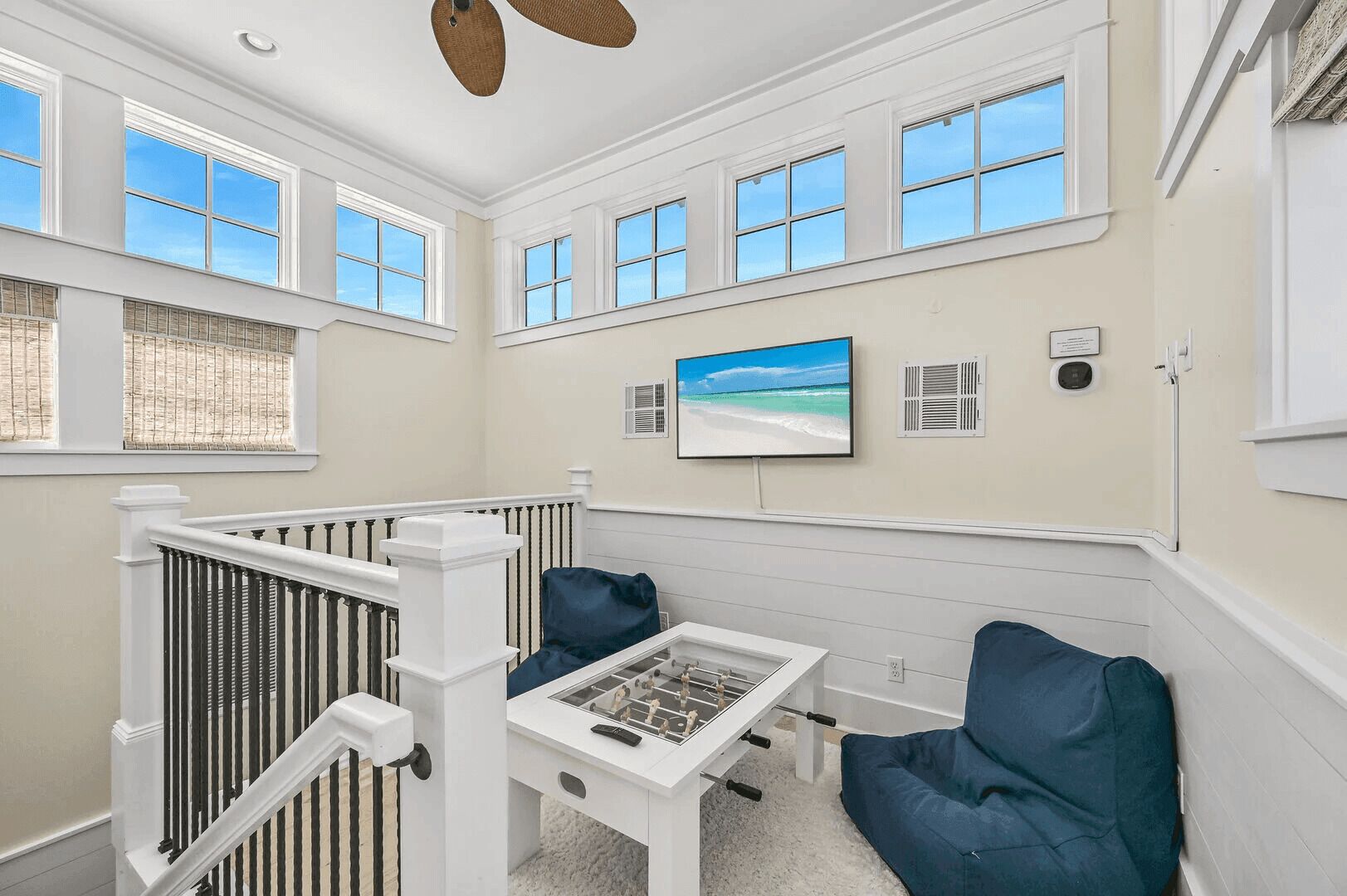 A room with a high ceiling, large windows, a foosball table, and a view of the beach.