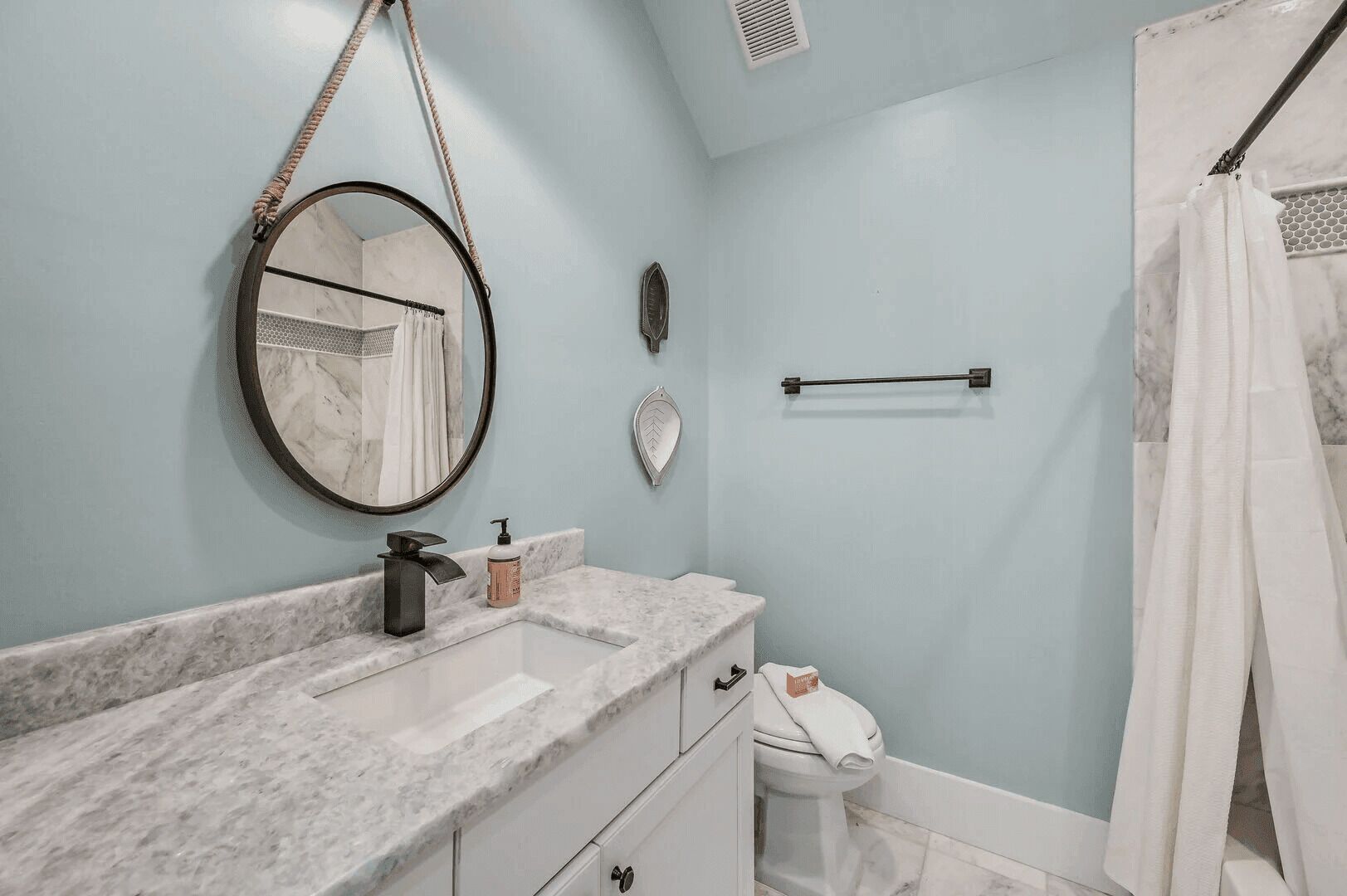 A bathroom with a marble sink, a round mirror, a towel rack, and a shower curtain.