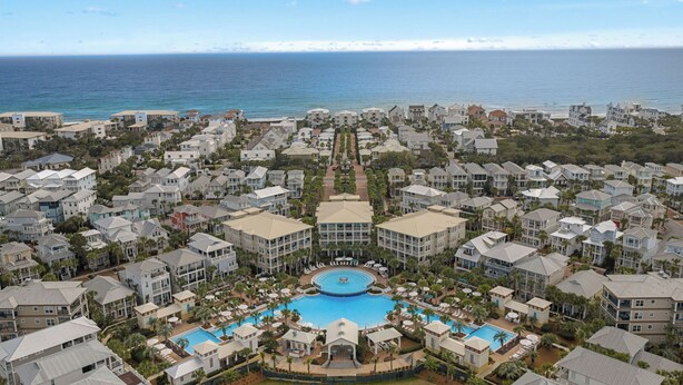 A resort with a central pool, multiple buildings, and a view of the ocean.