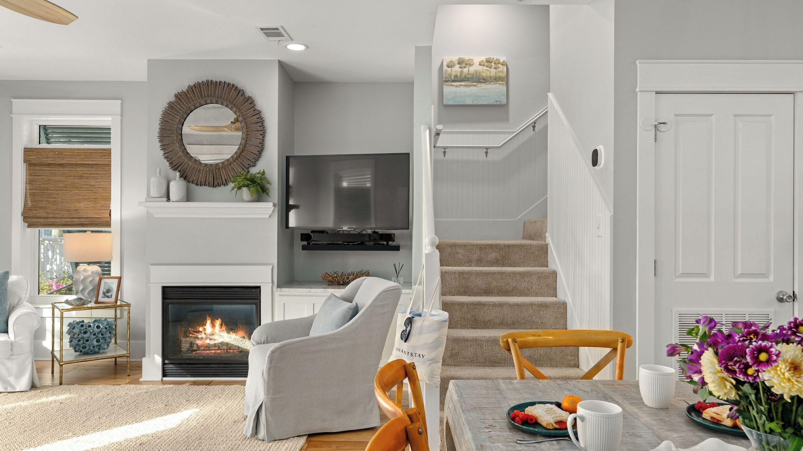 Una sala de estar con chimenea, televisor, escalera y comedor con mesa y sillas.