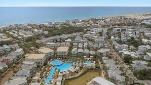 A coastal residential area with a large swimming pool surrounded by houses and a beach in the background.