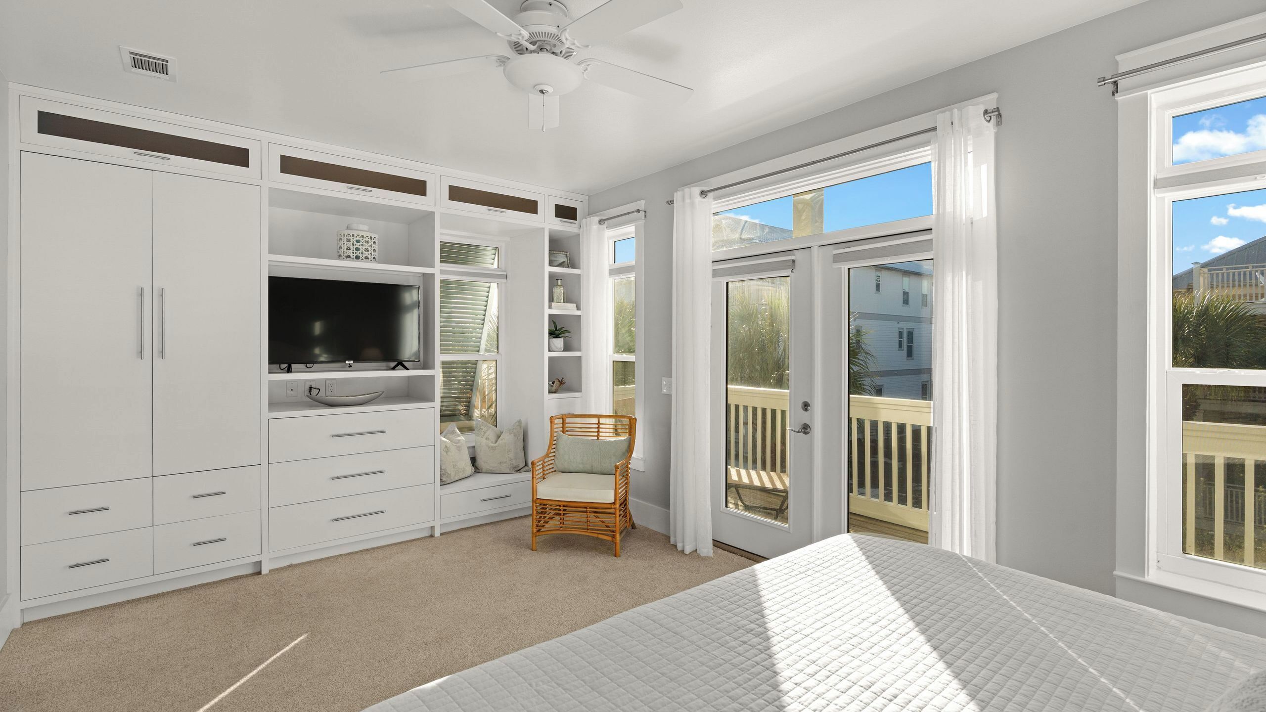 A bedroom with a bed, a television, a chair, and a sliding glass door to a balcony.