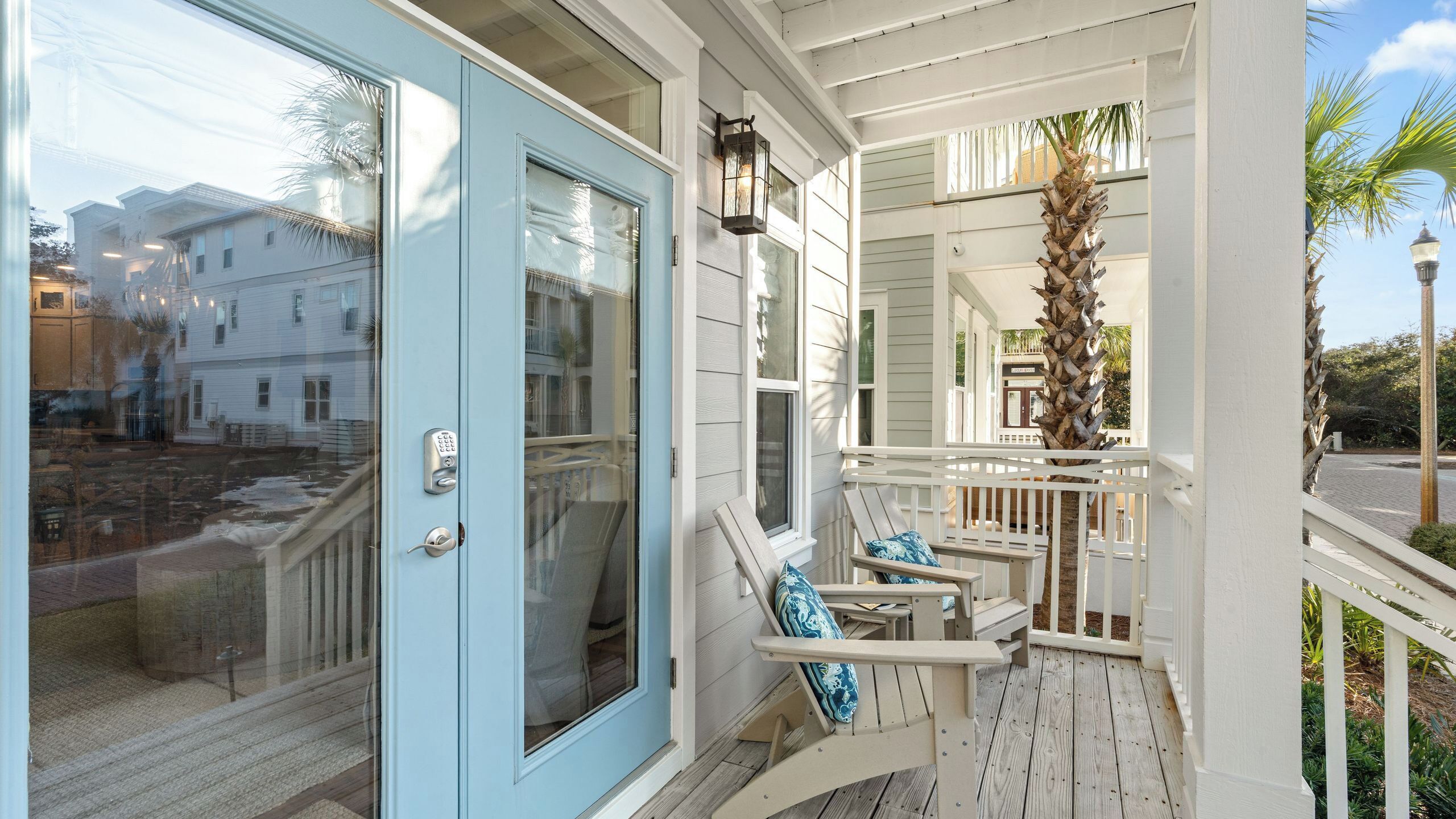 A porch with a blue door, a white railing, and two lounge chairs with blue cushions.