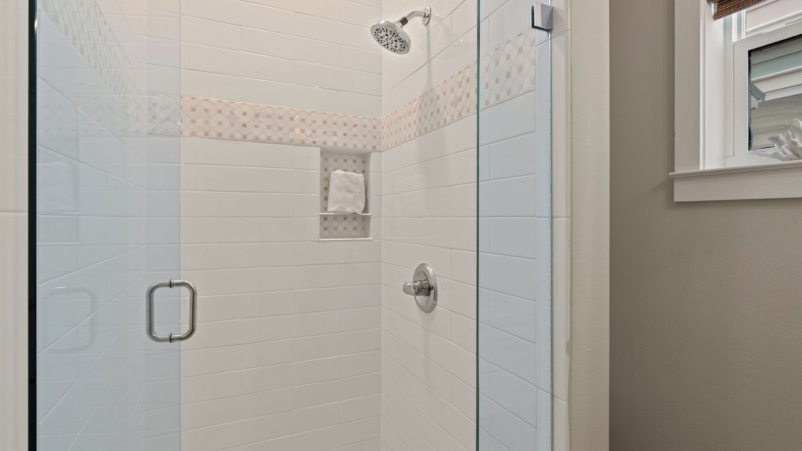 A shower with a handheld showerhead, a glass door, and a towel rack.