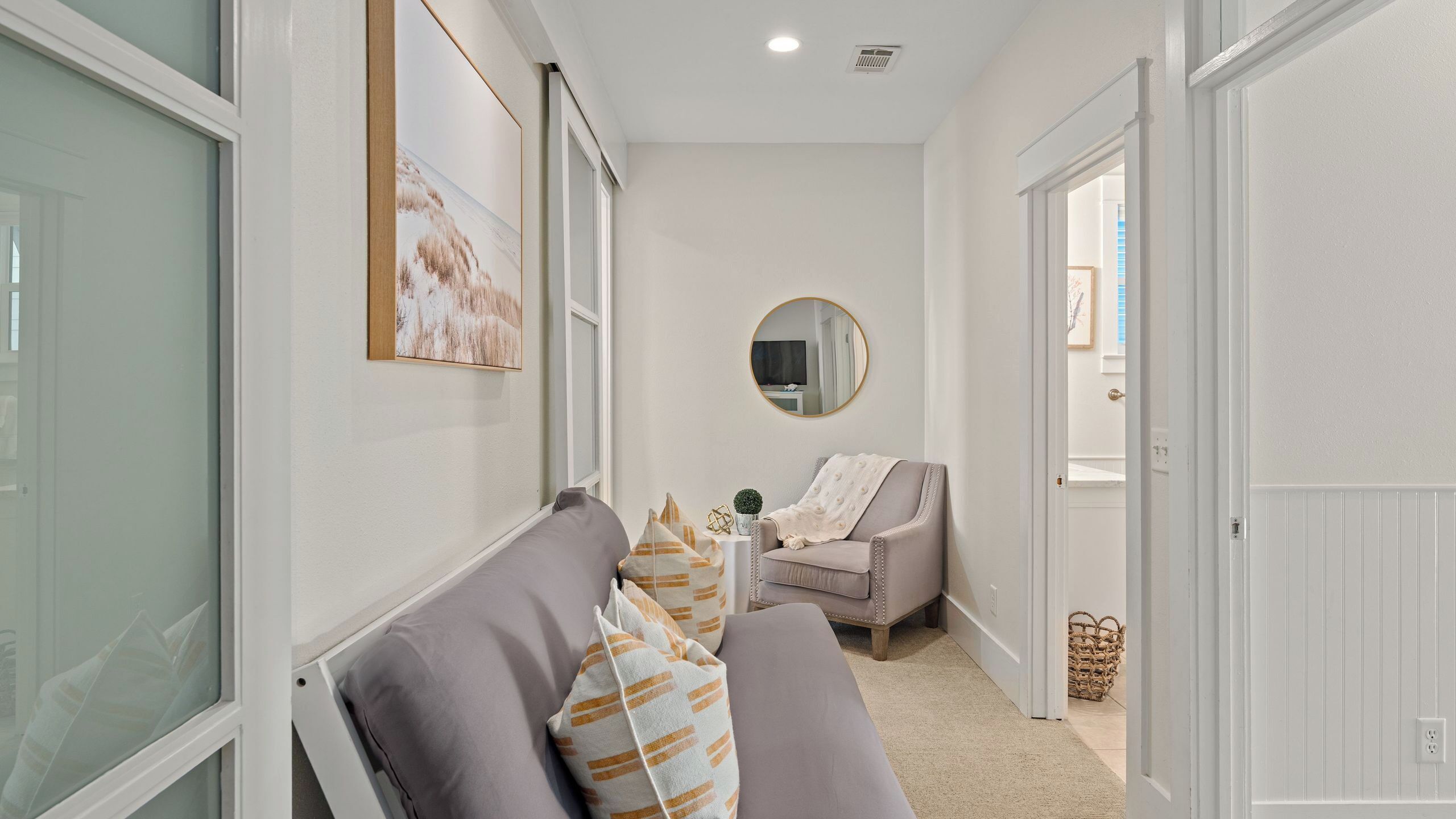 A hallway with a gray sofa, a round mirror, and a small table with decorative items.