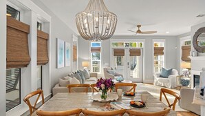 A spacious living room with a dining table, chairs, a chandelier, and a ceiling fan.