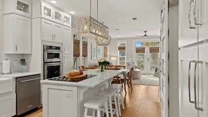 A modern kitchen with white cabinetry, a central island, and a dining area with wooden chairs.