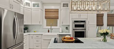 A modern kitchen with white cabinetry, stainless steel appliances, a central island, and a hanging light fixture.