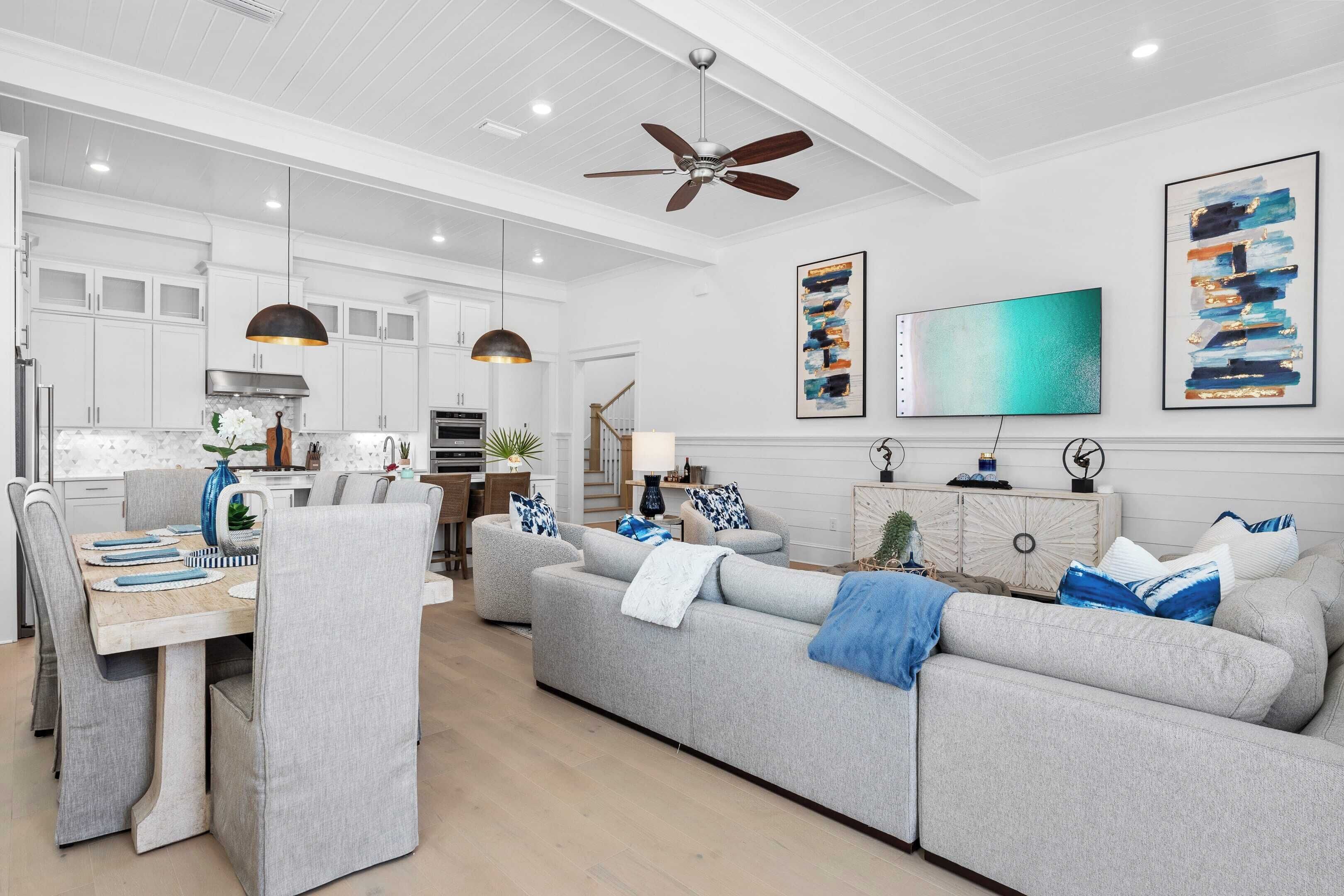 A modern kitchen with white cabinets, a dining area with a table and chairs, and a grey sofa in a living area.