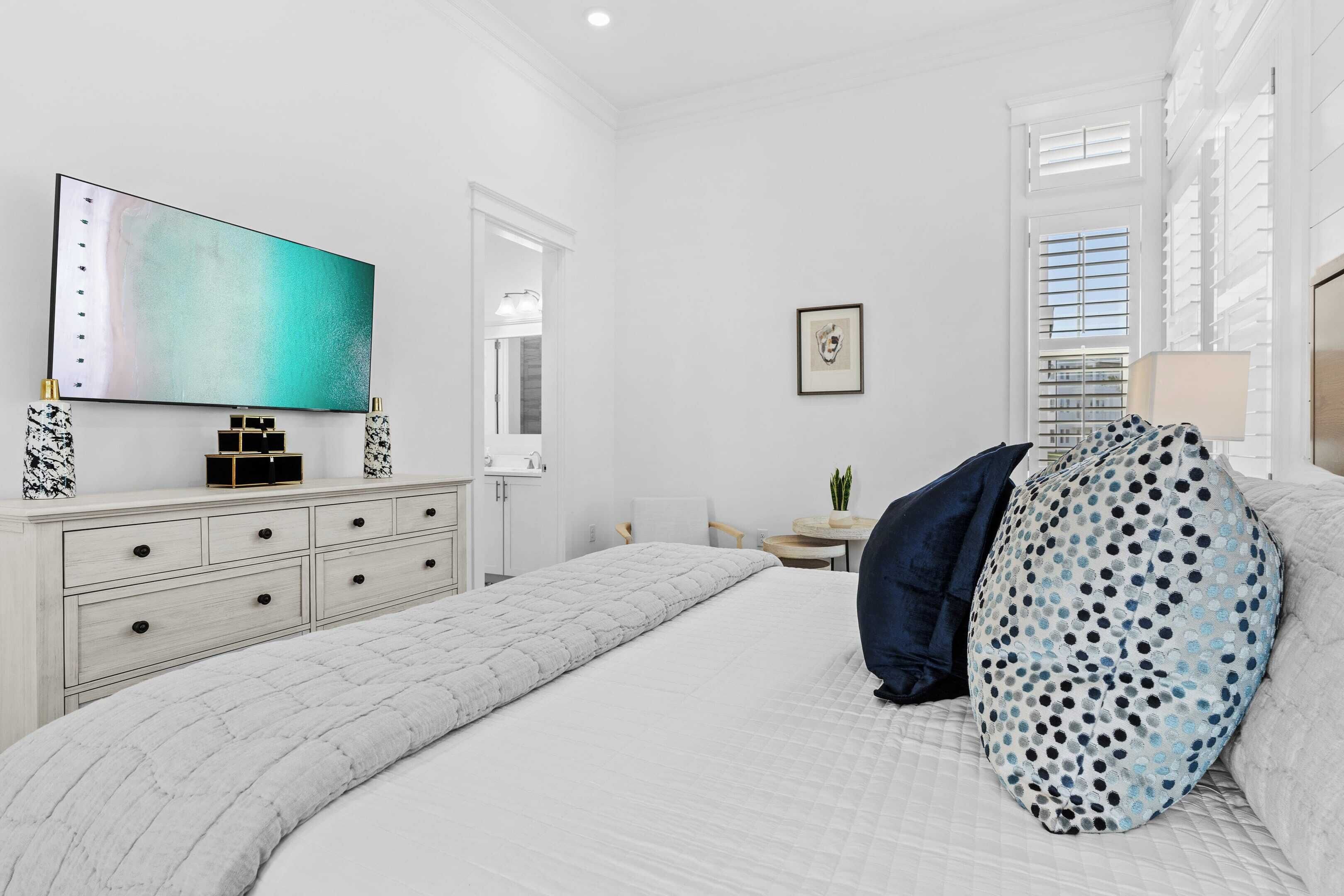 A bedroom with a bed, a TV, a dresser, and a window.